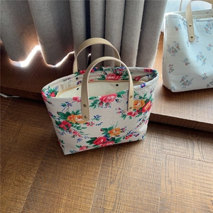 Detail of floral tote bags with leather handles and rivets on dark wooden floors