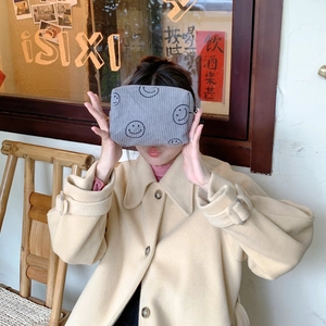 Detail of gray corduroy makeup bag featuring an embroidered smiley face held by a model