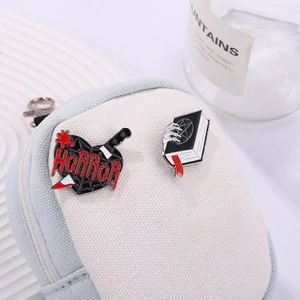 Dark gothic enamel pin set featuring a horror heart dagger and magic book on a canvas bag