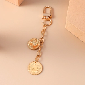 Golden double-coin pendant keychain with Elizabeth II portrait on beige background