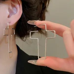 Boucles d'oreilles minimalistes en forme de croix argentée portées par un mannequin