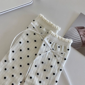 Detail of white knit crew socks featuring black polka dots and a silk ribbon bow ruffle cuff