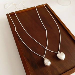 Colliers avec pendentifs cœur et goutte d'eau en argent brossé sur plateau bois