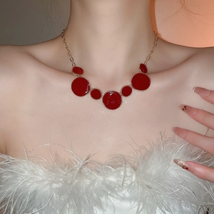 Détail d'un collier doré avec pendentifs circulaires rouges porté par un mannequin
