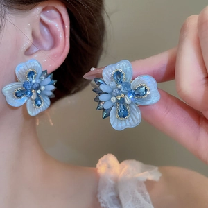 Detail of blue crystal flower earrings with pearls and gold edges on model