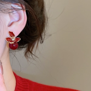 Close-up of elegant red flower earrings with gold accents and dark red beads on a model