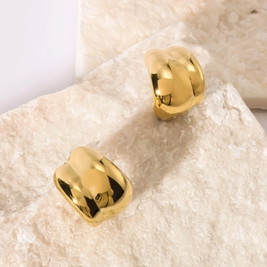 Polished gold C-shaped twisted stainless steel earrings on a white mineral stone