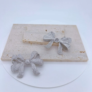 Elegant silver bow pendant connector with sparkling crystals on a textured marble surface