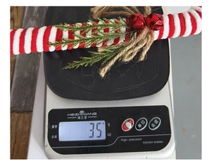 Macro view of a 35g red and white knitted candy cane ornament with bells and pine needles