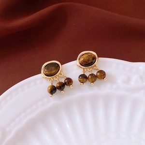 Close-up of vintage gold earrings with oval stone and triple beaded fringe on a ceramic plate