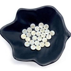 Perles en nacre naturelles avec lettres alphabet dorées sur un plateau noir mat