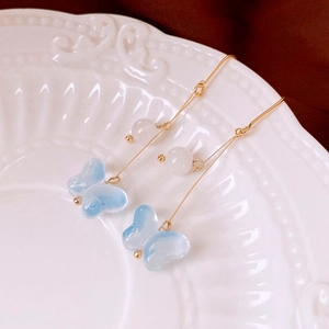 Détail de boucles d'oreilles papillon en verre bleu clair avec perles et glands dorés