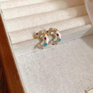 Polka dot C-shaped hoop earrings in cream enamel with vintage gold accents on fabric background