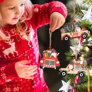 Three festive wooden Christmas truck ornaments being hung on a tree by a child
