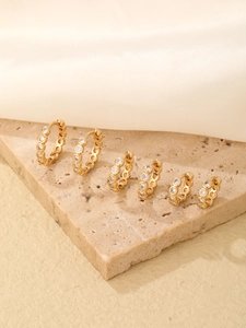 Three pairs of gold hoop earrings with micro-inlaid cubic zirconia on a beige stone