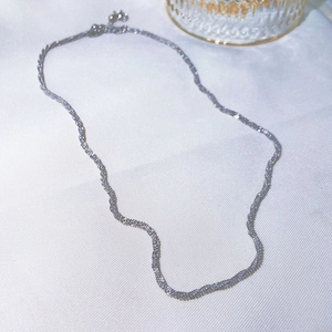 Detailed close-up of a silver titanium steel chain necklace on a white fabric surface