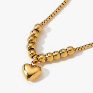 Polished gold heart pendant necklace with box chain and round beads on white background