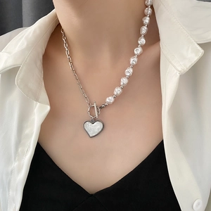 Elegant heart pendant necklace featuring half pearls and silver chain on a model