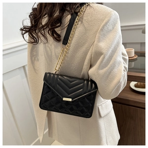 Vue latérale d'une femme portant un sac bandoulière en cuir noir surpiqué avec chaîne en métal