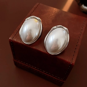 Detailed macro of oval pearl earrings in textured silver frames on leather display