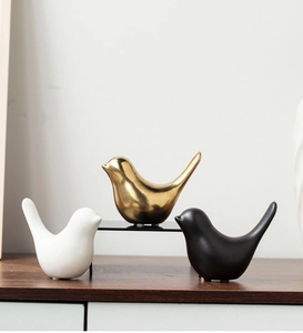 Trio of decorative ceramic birds in gold, white, and black on a wooden tabletop