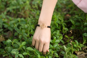 Detail of beaded bracelet featuring a gold hollow cross pendant with sparkling crystals