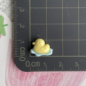 Miniature yellow resin duck figurine on blue wave base showing 1.5cm size scale