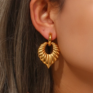 Close-up of golden leaf pendant earrings with radial texture worn on ear