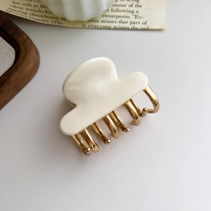 Detail of cream acetate and gold metal claw clip on a minimalist aesthetic background