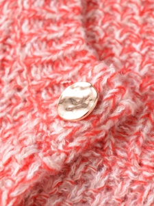 Close-up of golden hammered metal button on thick orange and white knit fabric