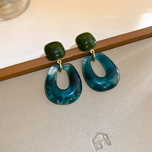 Close-up of geometric marble resin earrings with wood texture on a leather surface