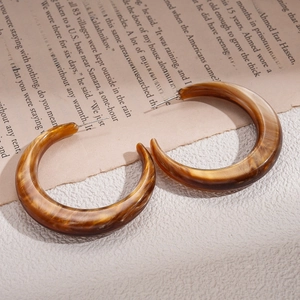 Close-up of amber resin C-shape hoop earrings with marbled texture on retro paper