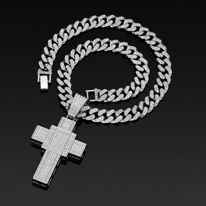 Detailed close-up of a silver-tone iced out cross pendant on a rhinestone Cuban chain