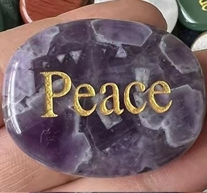 Macro shot of a purple amethyst stone with gold Peace engraving held in hand