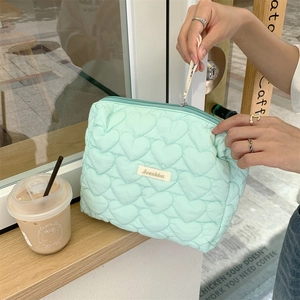 Detail of mint green heart quilted cosmetic bag resting on a wooden cafe windowsill