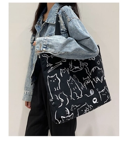 Close-up of black canvas tote bag with white cartoon cat pattern worn over the shoulder