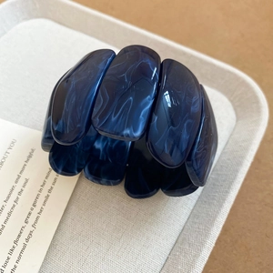 Detailed view of a wide dark blue marble resin bead bracelet on a beige textured tray