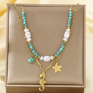 Détail de pendentifs étoile de mer et hippocampe dorés avec perles sur collier étagé