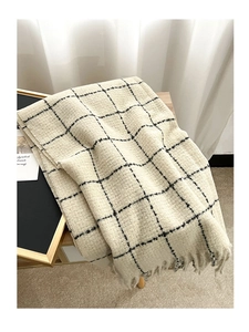 Detail of soft black and white plaid scarf with long fringes on a wooden chair