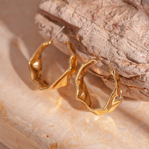 Macro shot of gold pleated C-shaped hoop earrings with liquid metal texture on stone