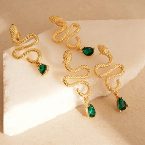 Golden snake-shaped drop earrings with green pear-cut crystal charms on stone blocks
