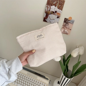 Detail of hand holding a beige corduroy pouch with a woven label on a cozy desktop