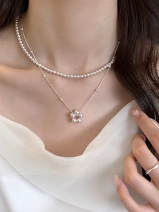 Détail de colliers de perles superposés et pendentif floral délicat sur la clavicule