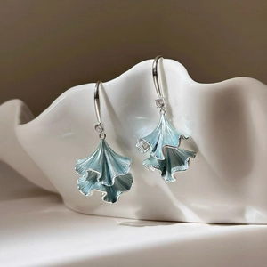 Detailed close-up of blue ginkgo leaf earrings with zircon accents on a porcelain dish
