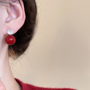 Close-up of red heart pearl earrings with silver needles and crystal studs on a model
