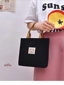Detailed view of black canvas tote bag with a bear patch and durable khaki handles