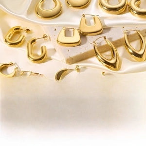Polished gold titanium steel hollow hoop earrings displayed on white silk and marble