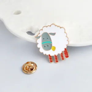 Detail of a cute cartoon sheep enamel pin with a gold butterfly clutch on a white plate