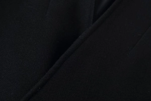 Gros plan sur la texture du tissu en laine noire et les détails de couture du manteau