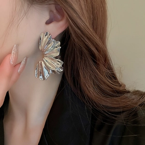 Close-up of oversized silver fan-shaped metal earrings with pleated texture on model